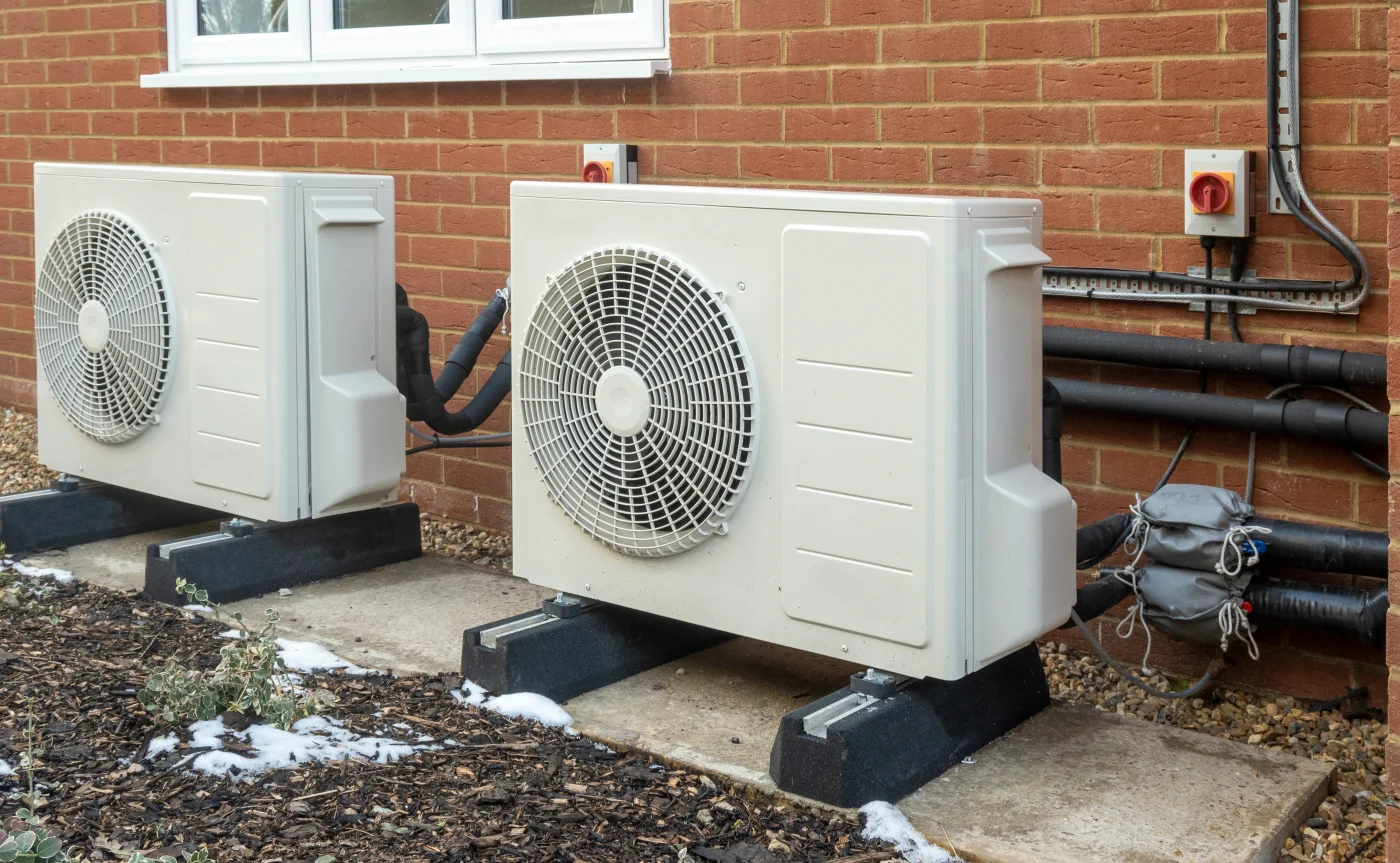 Two outdoor heat pump units next to a brick home