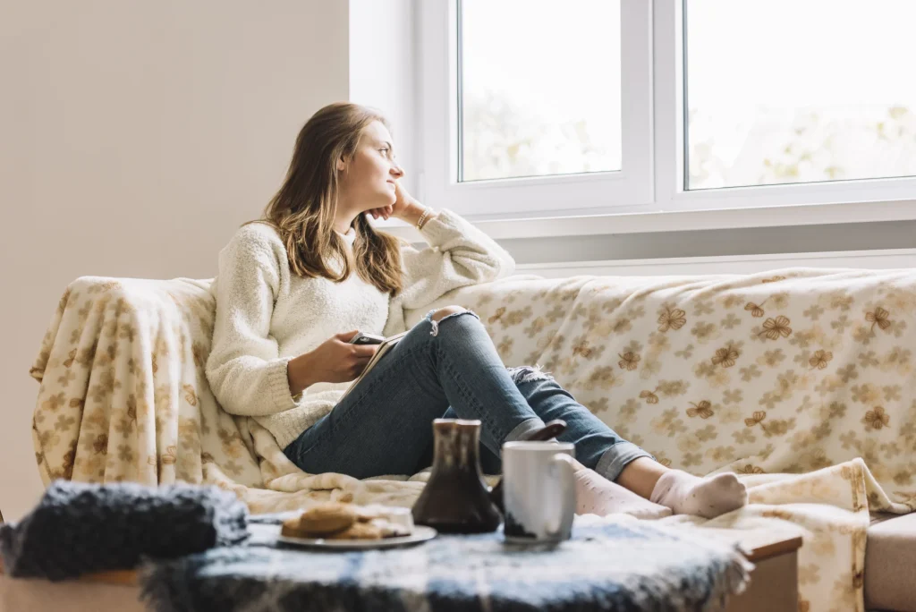 A woman on a couch looking outside while on her mobile phone.